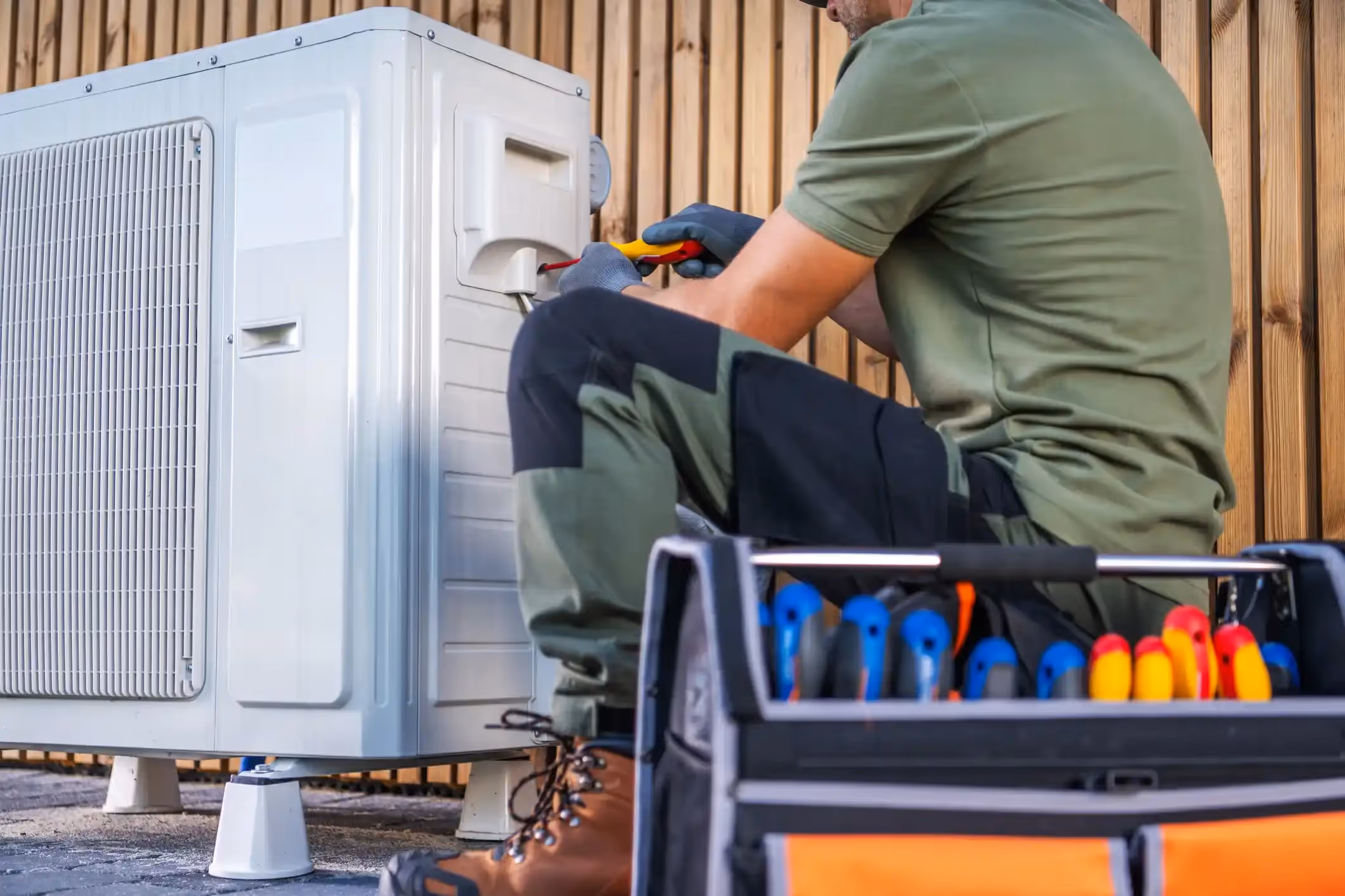 Close-up of an HVAC technician working on an outdoor air conditioning unit with tools in a toolbox.