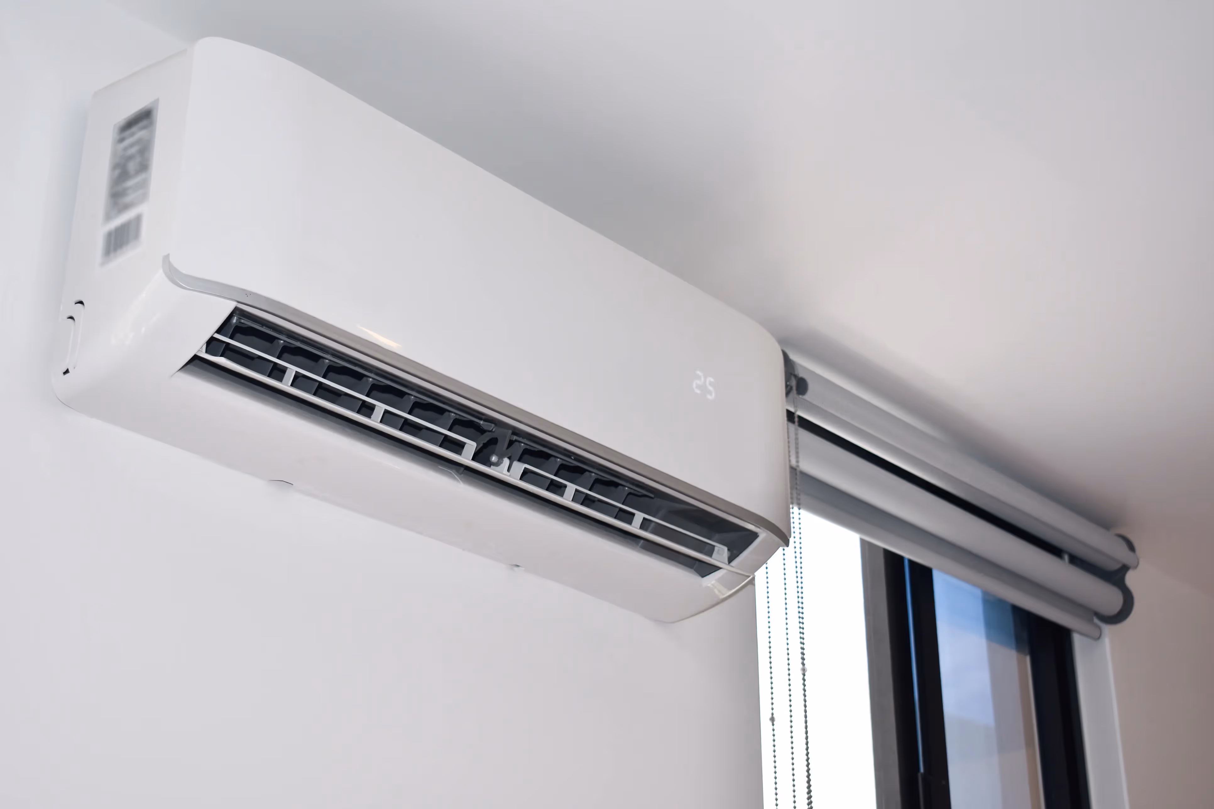 A modern white ductless air conditioner is mounted on a wall above a window.