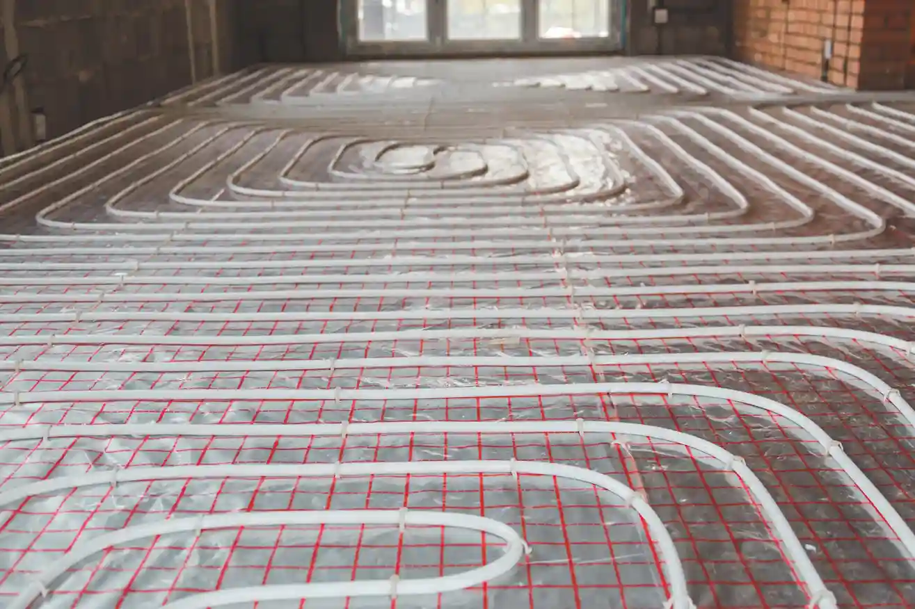 A low-angle view of white radiant heating pipes installed in a looping pattern on a gridded mat, ready for a concrete floor to be poured.