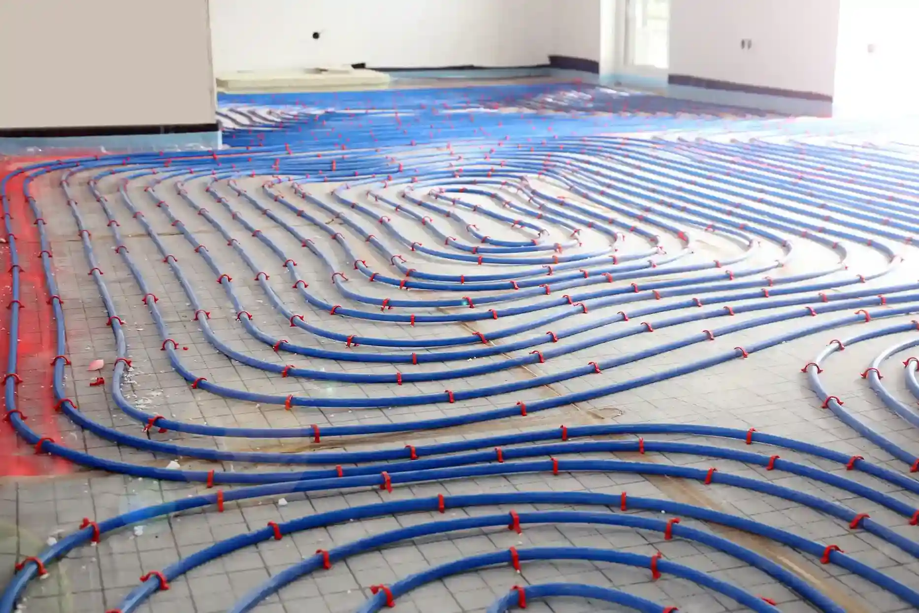 A low-angle shot of a floor under construction with blue radiant heating pipes laid in a looping pattern on a gray mat.