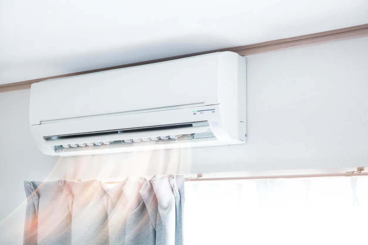 Wall-mounted air conditioner above a window with flowing curtains. 
