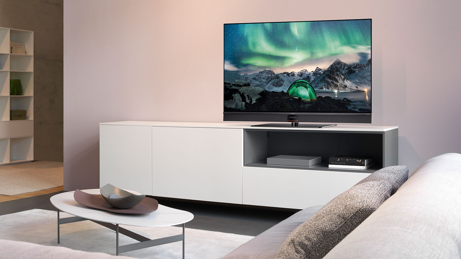 Metz Fernseher auf weißem Sideboard, zeigt ein Nordlicht über einer verschneiten Berglandschaft