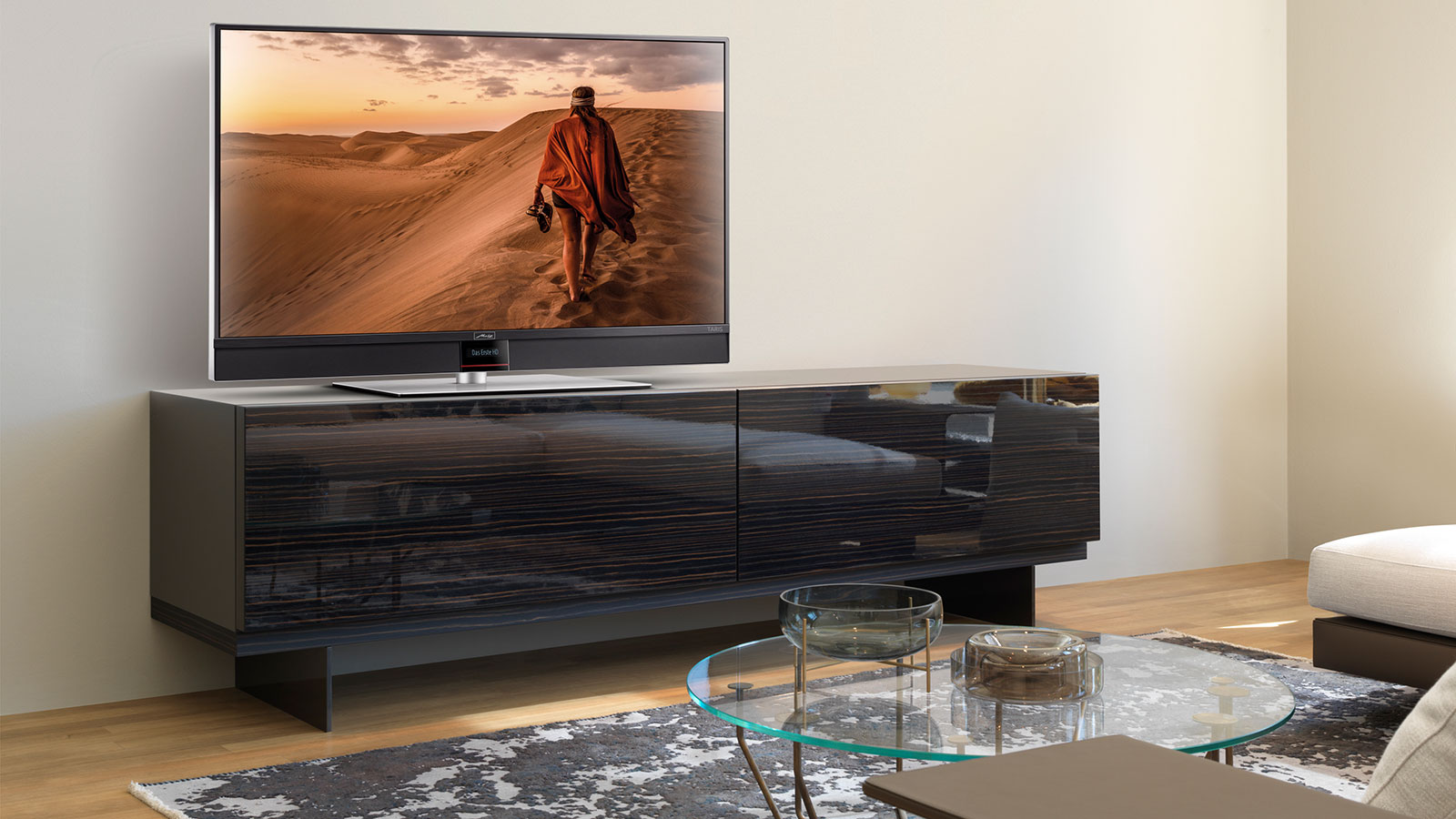 Metz Fernseher auf einem dunklen Lowboard, zeigt eine Wüstenlandschaft mit einer gehenden Person