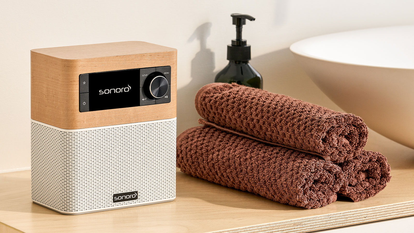 Kompaktes Sonoro-Radio mit Holzoberseite auf einem Badregal neben drei gerollten braunen Handtüchern