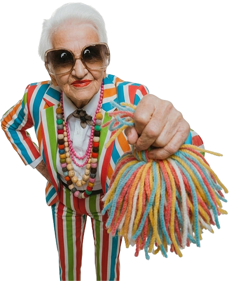Elderly woman wearing vibrant geometric-patterned clothes, a lime green vest, chunky necklace, sunglasses, and smiling with one arm raised.