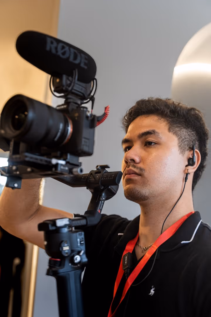 Young man wearing earphones operates a camera rig with mounted RØDE microphone.