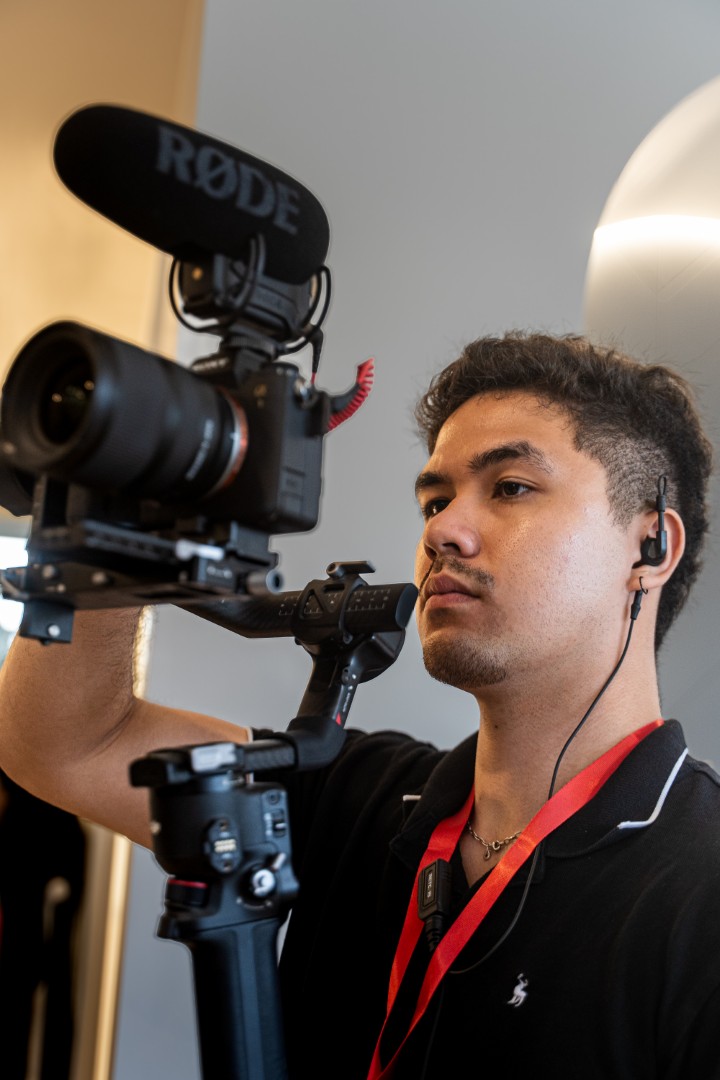 Young man wearing earphones operates a camera rig with mounted RØDE microphone.