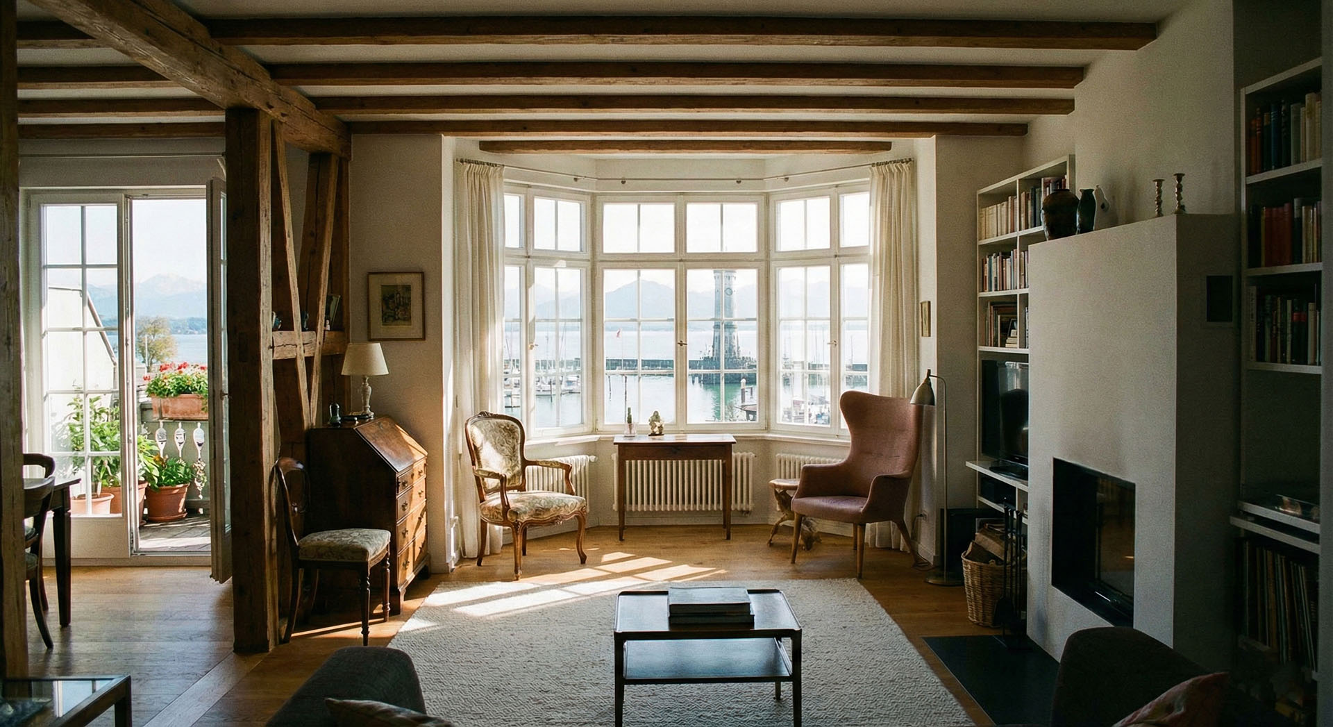 Helles Wohnzimmer mit Holzbalkendecke, antiken Stühlen, Kamin und großen Fenstern mit Blick auf einen Hafen und Berge.