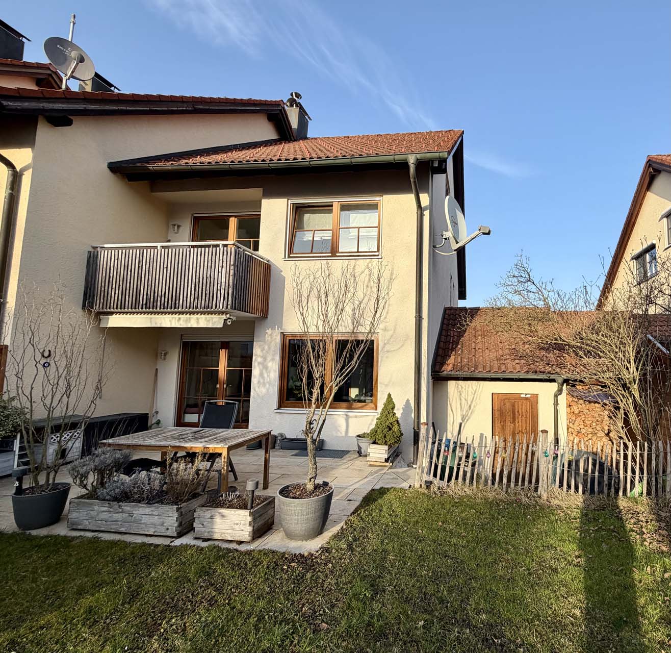 Blick von einer Dachterrasse mit Metallgeländer auf Häuserdächer und kahlen Baum bei bewölktem Himmel.