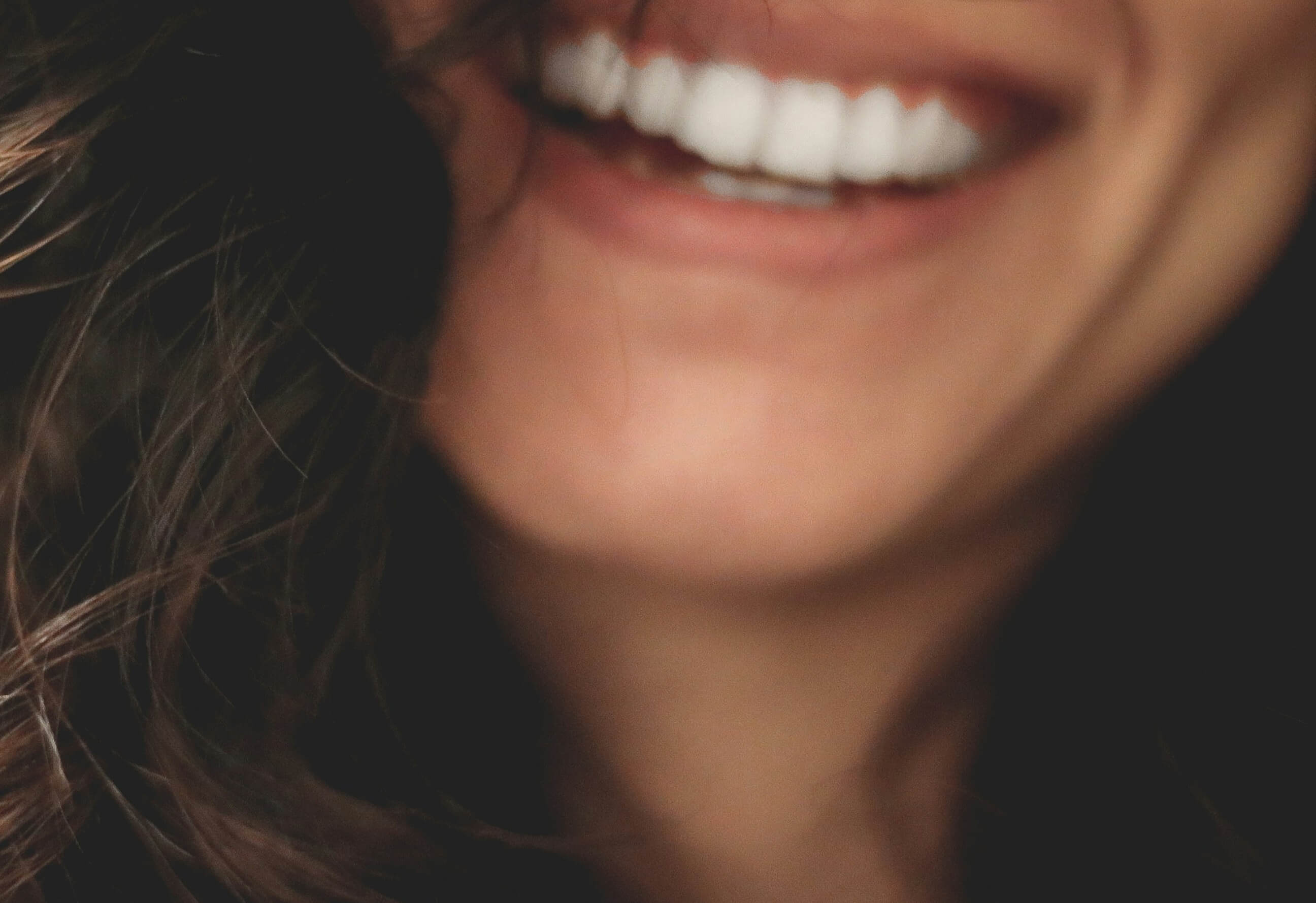 Bild Nahaufnahme eines lächelnden Mundes mit weißen Zähnen und braunen Haaren.