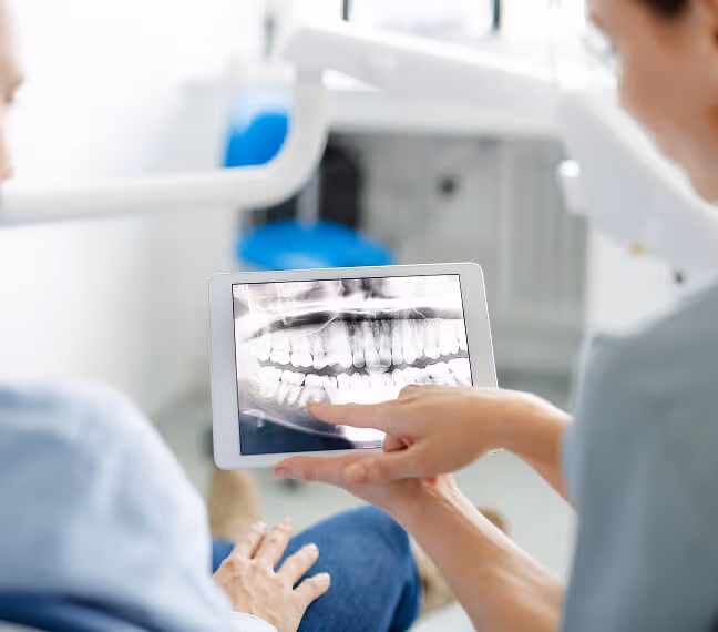 Bild Zahnärztin zeigt einem Patienten auf einem Tablet eine digitale Röntgenaufnahme des Kiefers mit Zähnen.