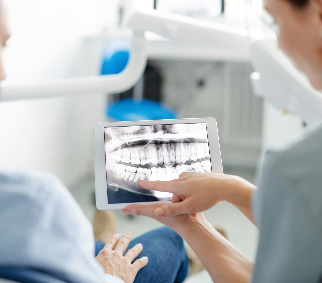 Bild Zahnärztin zeigt einem Patienten auf einem Tablet eine digitale Röntgenaufnahme des Kiefers mit Zähnen.