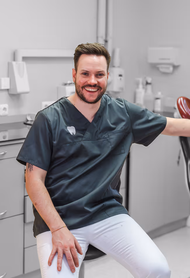 Bild Lächelnder Mann in Zahnmedizin-Uniform sitzt in einer modernen Praxis.