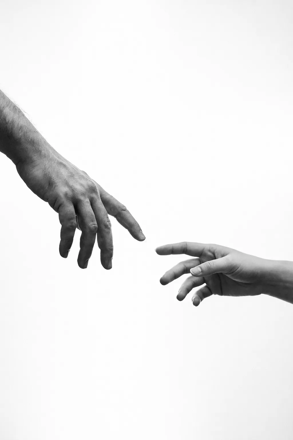 Black and white photo of two hands reaching toward each other against a white background.