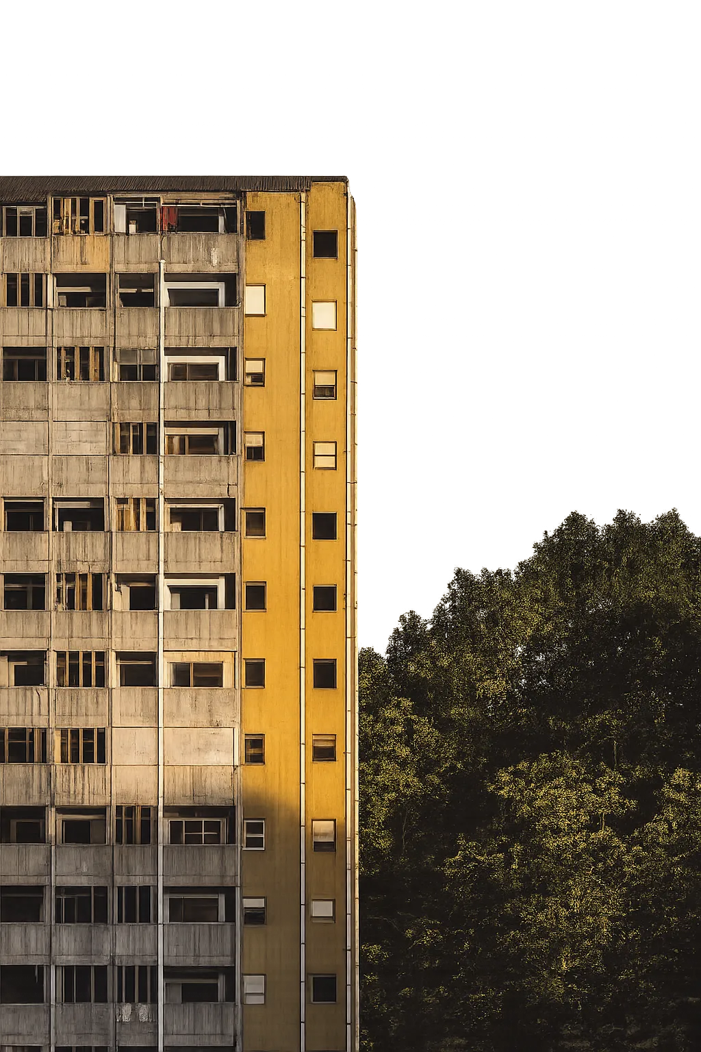 Side view of a tall building with gray and yellow facades beside a green tree cluster at dusk.