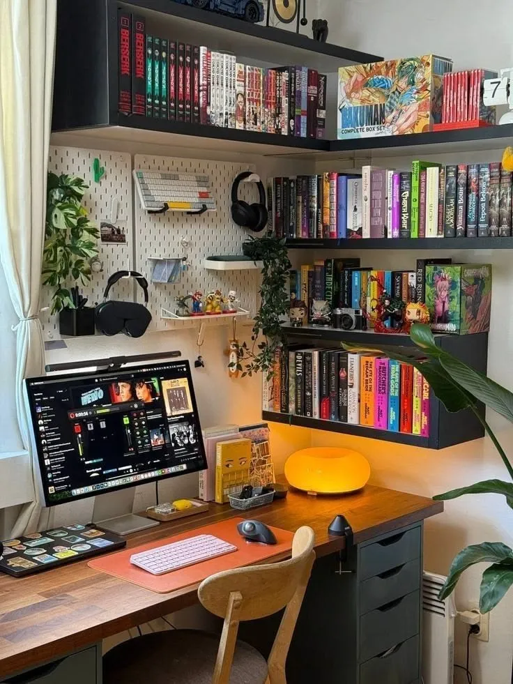 Desk setup with computer, keyboard, mouse, wall shelves with books, plants, and figurines in a cozy room.