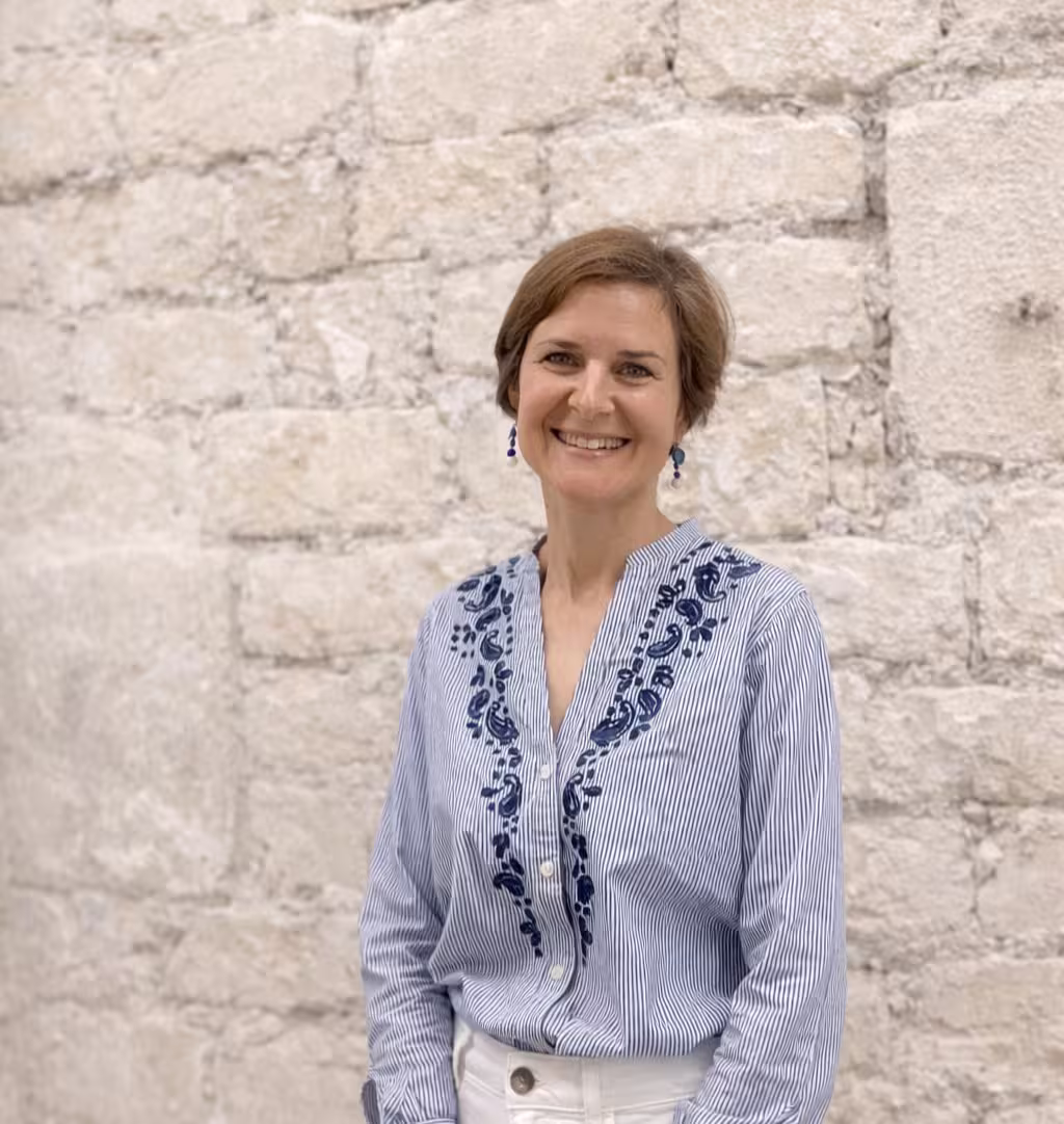 Middle-aged man with light beard and short hair wearing a white button-up shirt, standing outdoors with green foliage background.
