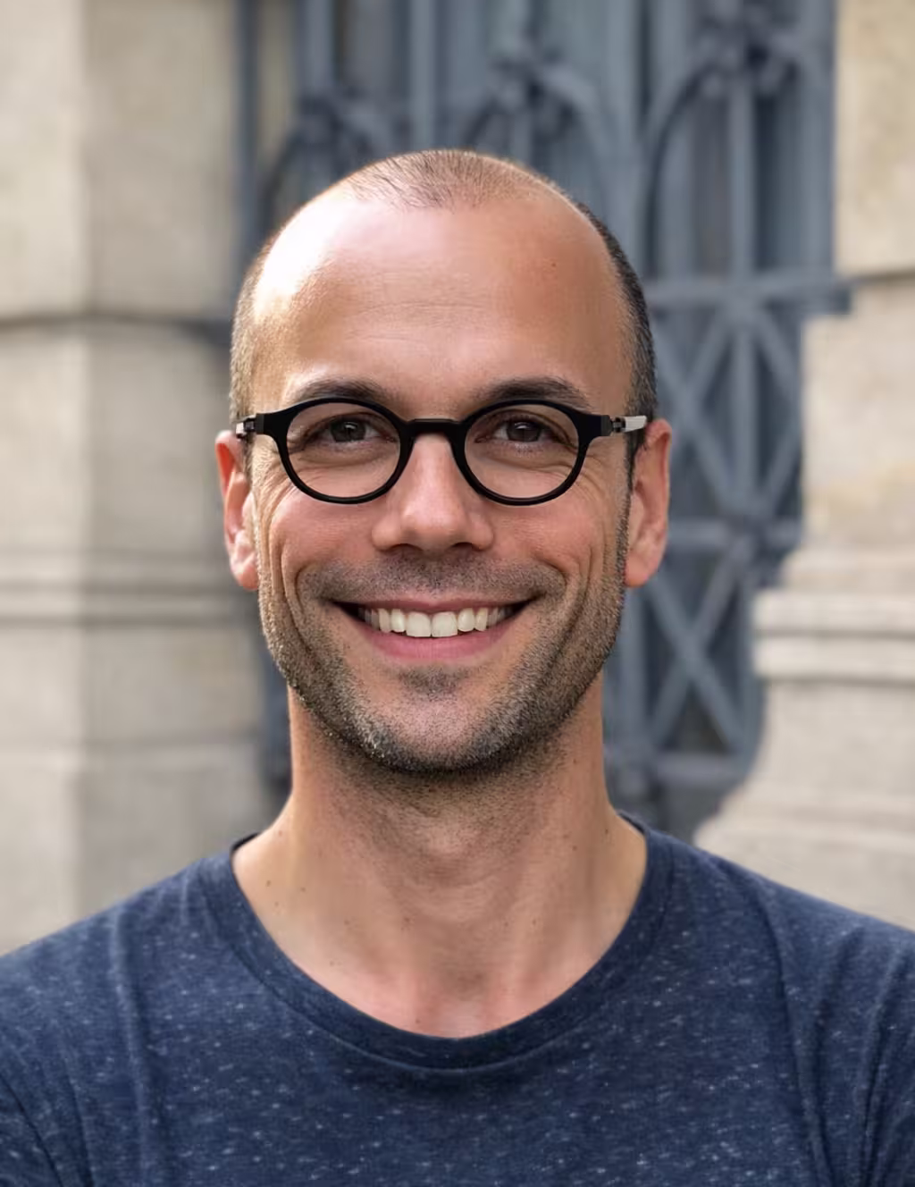 Middle-aged man with light beard and short hair wearing a white button-up shirt, standing outdoors with green foliage background.