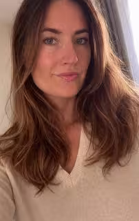 Middle-aged man with light beard and short hair wearing a white button-up shirt, standing outdoors with green foliage background.