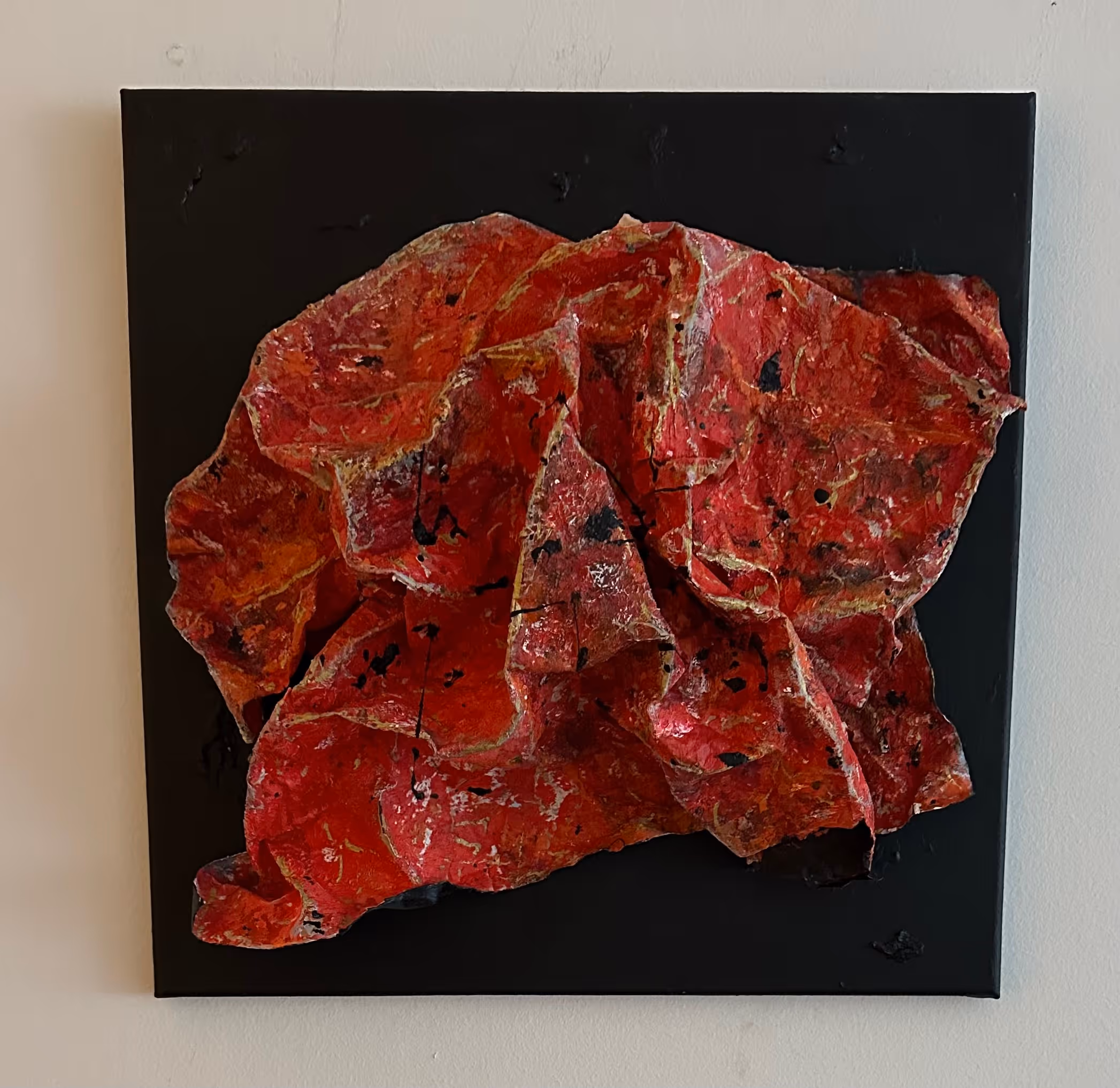 Abstract textured artwork featuring crumpled red and orange paper-like material on a black square canvas.