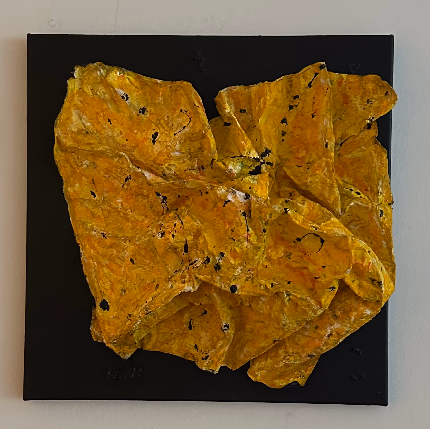 Abstract textured wall art featuring crumpled yellow-orange material with black speckles on a black square background.