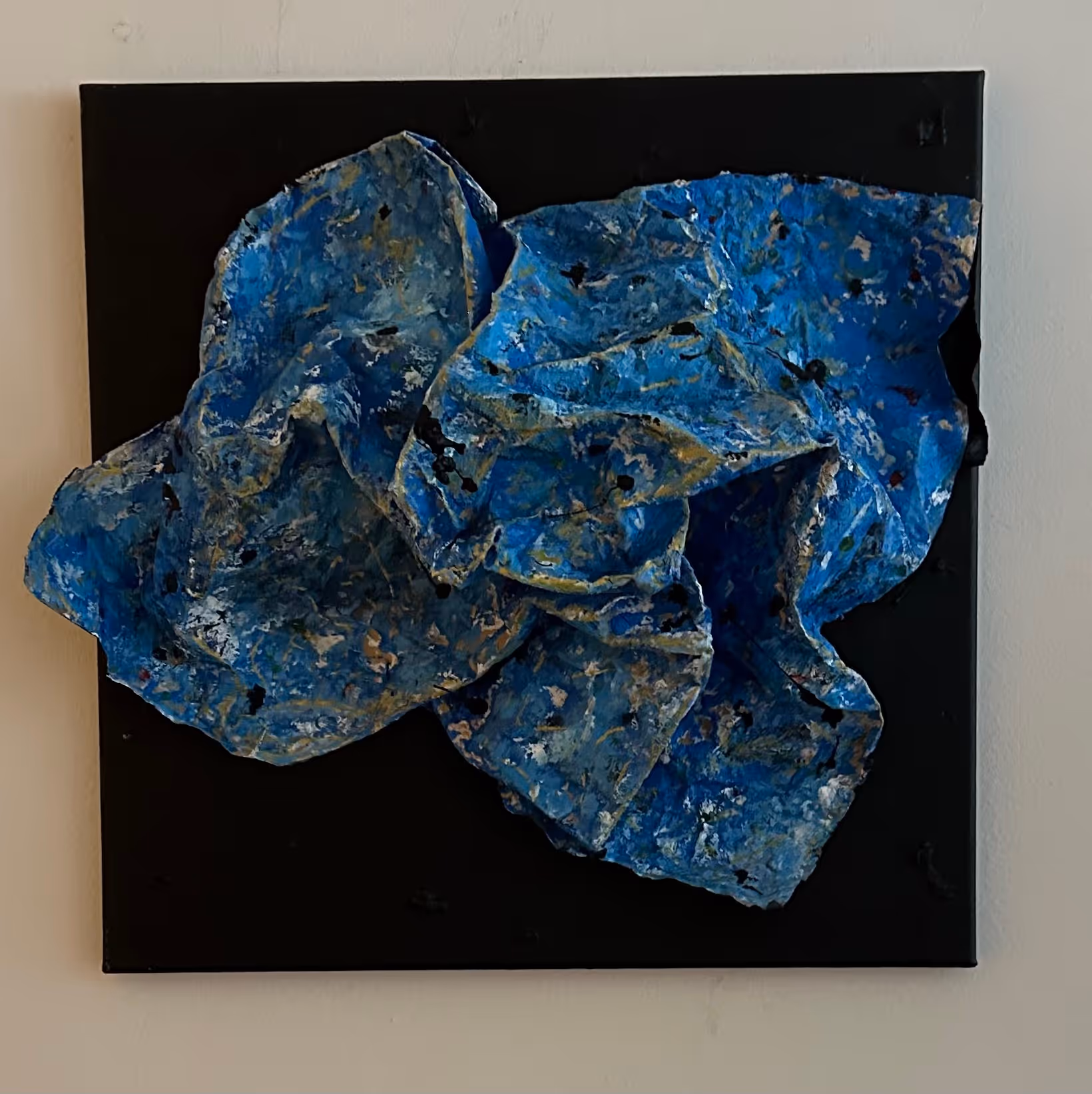 Abstract textured blue and gray sculpture mounted on a black square background.