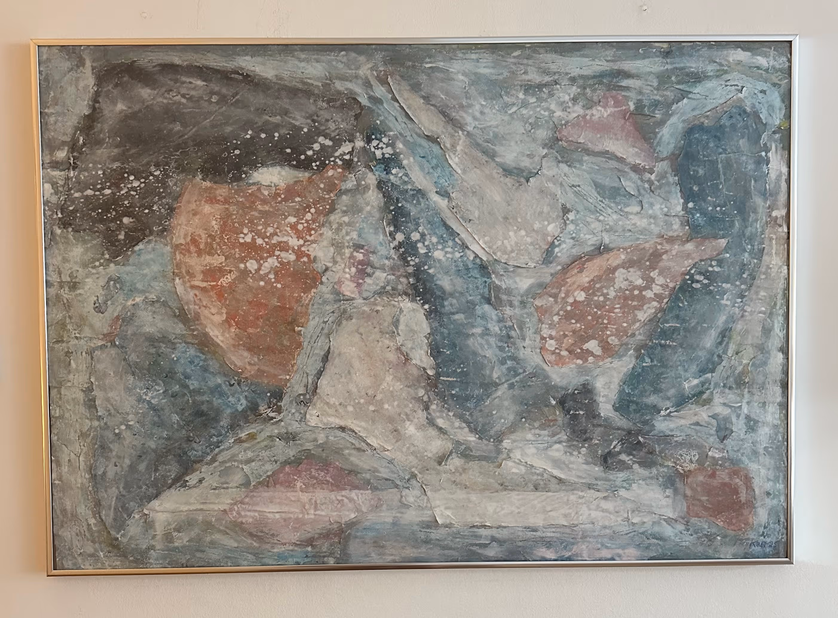 Abstract painting with layered shapes in muted blue, gray, red, and white tones with splattered white spots, framed and hung on a wall.