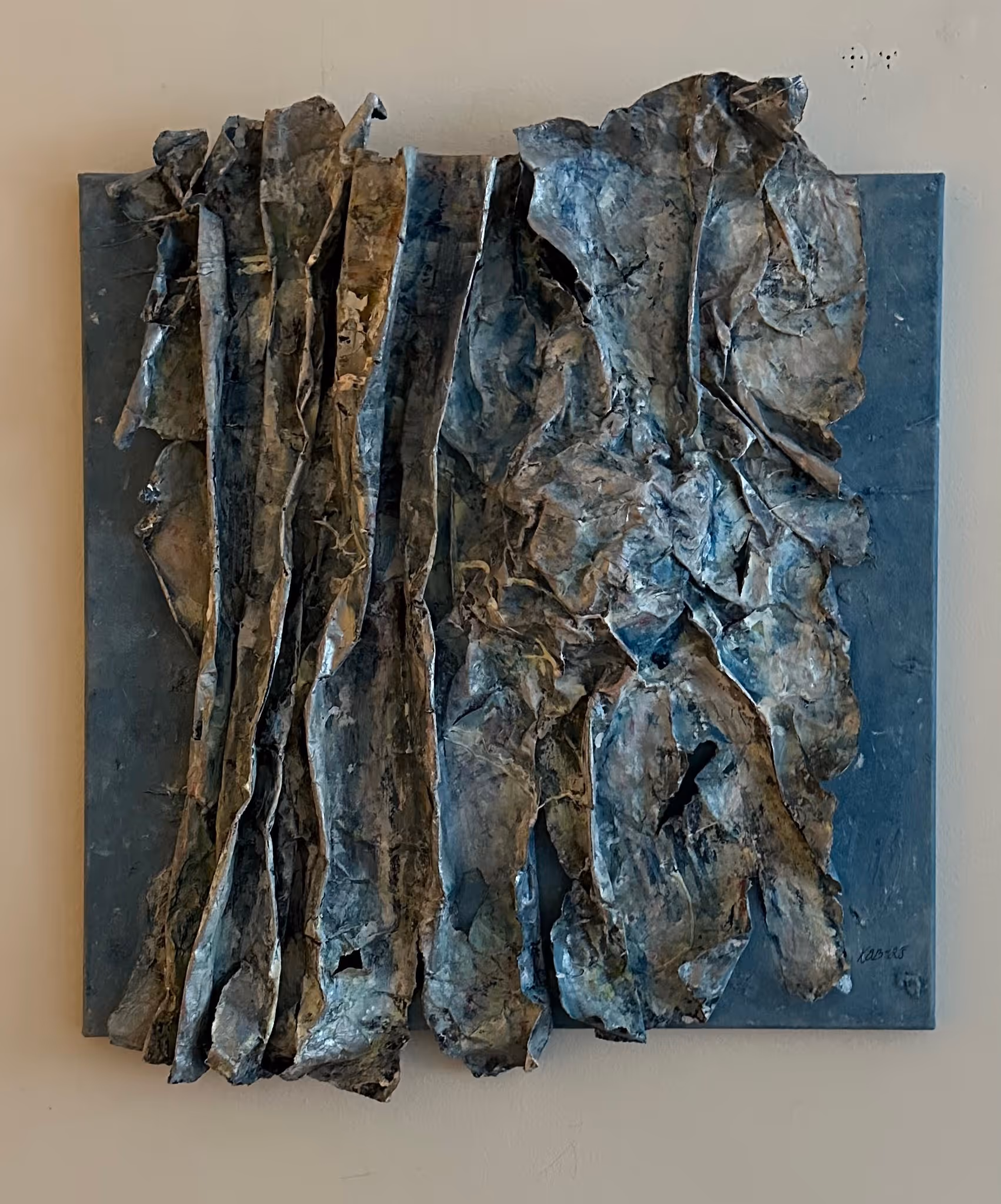 Abstract mixed media artwork with wrinkled, layered, and textured metallic-like sheets in dark blue and silver tones on a square background.