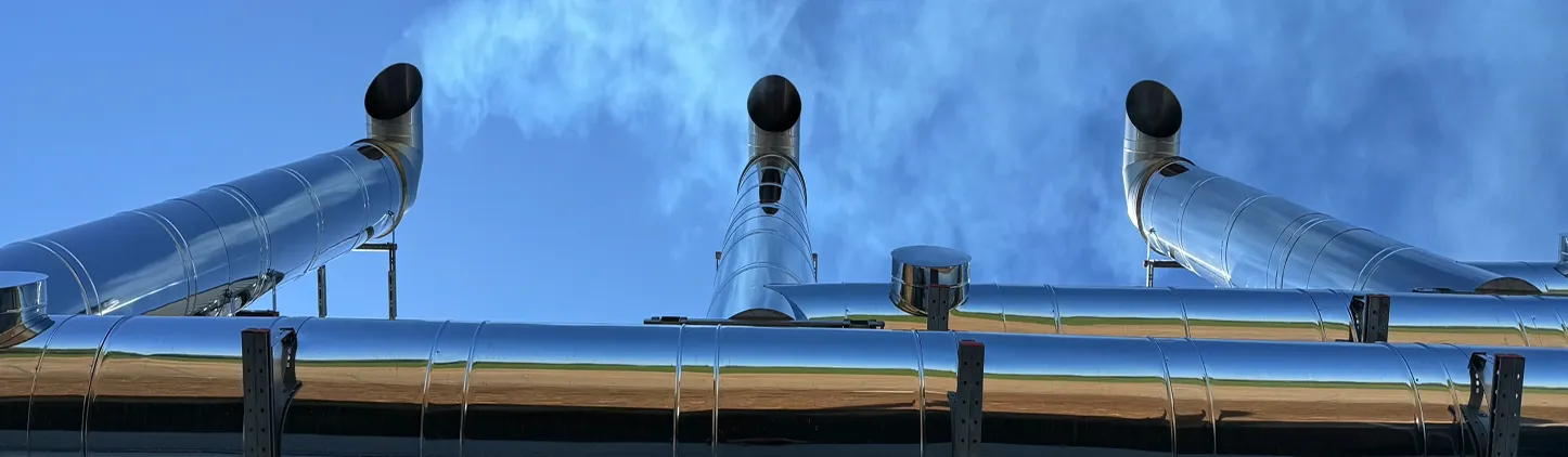 Tři vertikální kovové komíny s černými otvory v nich a modrá obloha v pozadí.