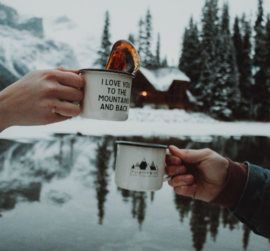 deux personne font santé avec deux tasses à la montagne sous la neige