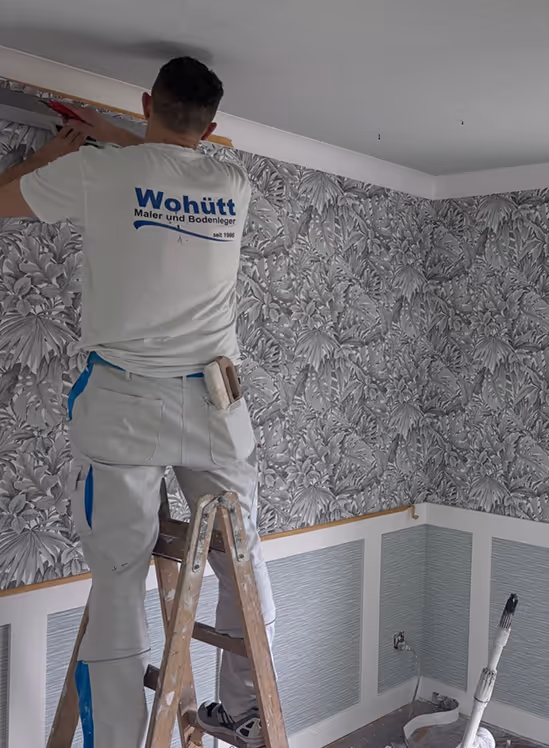 Mann steht auf einer Leiter und bringt Tapete mit floralem Muster an der Wand an.
