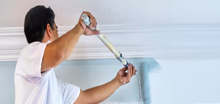 Mann bemalt Wand mit blauer Farbe und Farbroller.