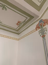 Ecke eines Raums mit klassischer Wand- und Deckenmalerei in Grün, Gold und Rot, inklusive floraler Motive.