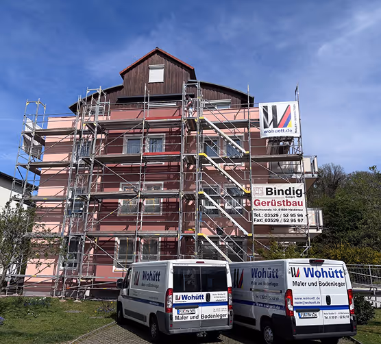 Wohnhaus mit Gerüst für Maler- und Bodenlegerarbeiten, davor zwei Lieferwagen mit Wohütt-Logo.