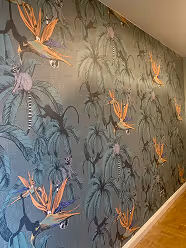 Wand mit Tapete, die einen tropischen Blumendruck mit orangefarbenen Strelitziablumen und grünen Palmenblättern zeigt.