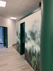 Flur mit hellen Böden, grünen Wänden und einem Waldbild an einer Wand.