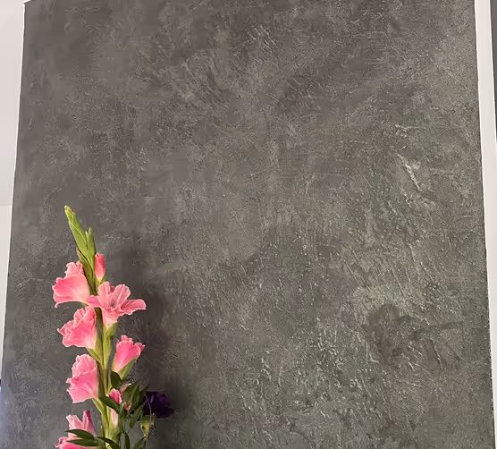 Ein Ast mit pinken Gladioolenblüten vor einem dunkelgrauen, strukturierten Hintergrund.