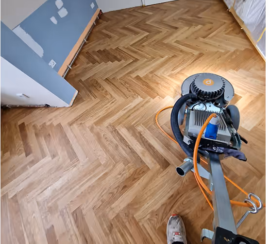 Parkettboden wird geschliffen mit einer Schleifmaschine in einem Raum mit blauen und weißen Wänden.