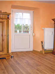 Helle Zimmertür mit Fenster, links ein hölzerner Schrank, rechts Heizkörper und Holzboden.