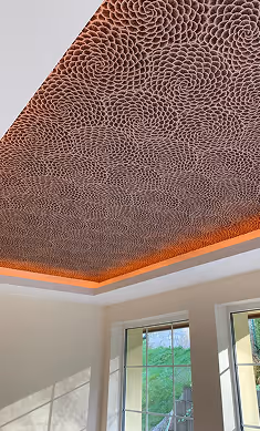 Zimmerdecke mit dekorativem Muster aus spiralförmigen Linien und warmem indirektem orangefarbenem Licht entlang der Ränder.