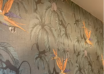 Wand mit Dschungel-Tapete mit Palmen, Vögeln und Schmetterlingen in gedeckten Farben.