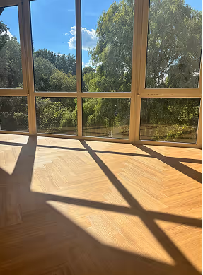 Sonnendurchfluteter Raum mit großen Fenstern, die einen Blick auf grüne Bäume und blauen Himmel bieten.