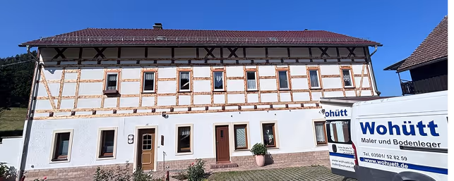 Traditional German half-timbered house with a tiled roof and two white Wohütt company vans parked in front.