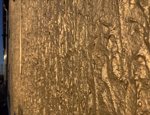 Nahaufnahme einer goldfarbenen, strukturierten Wand mit unregelmäßiger Oberfläche.