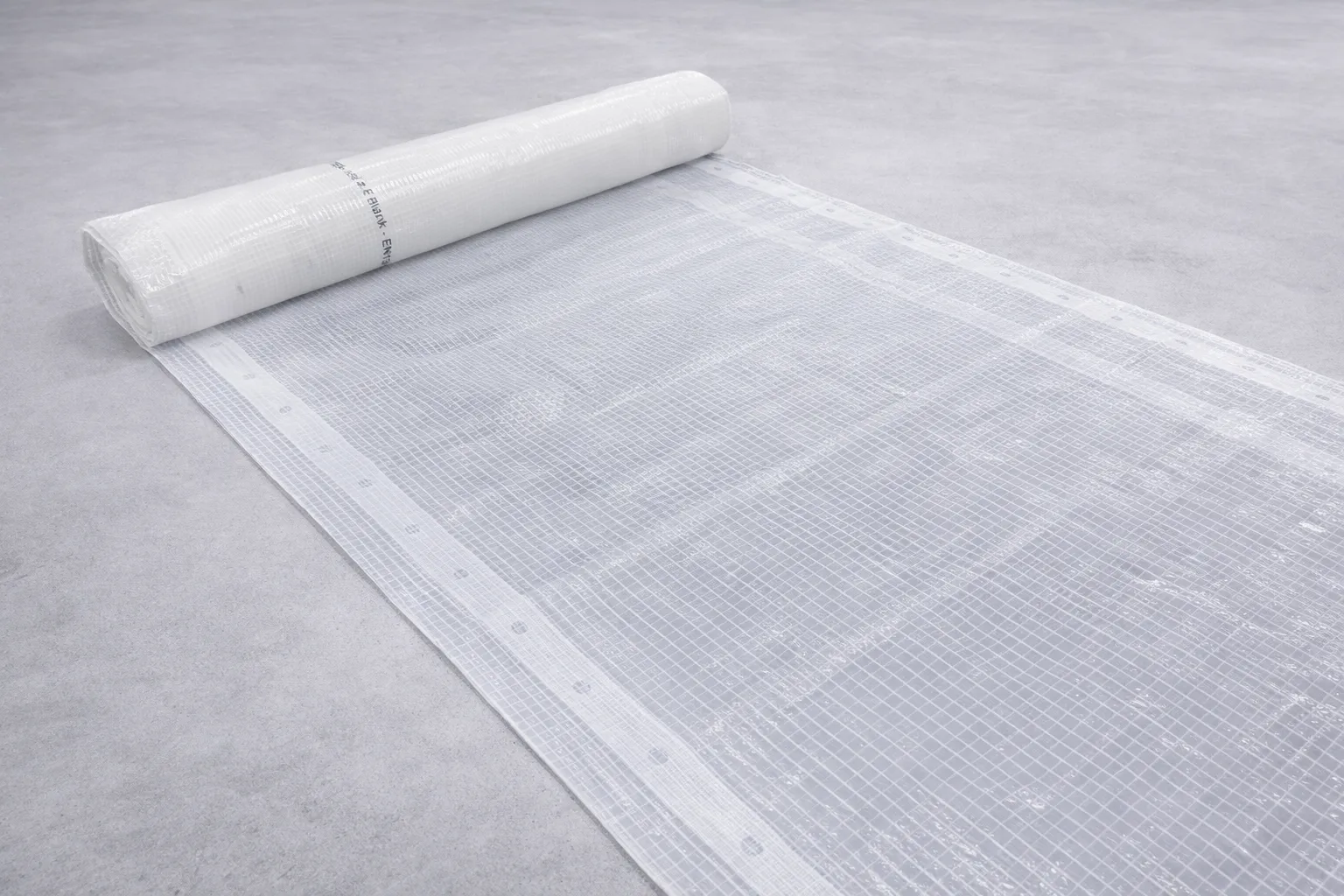 Rulle med gjennomsiktig, hvitt nettingmateriale med firkantmønster rullet ut på en glatt, grå overflate.