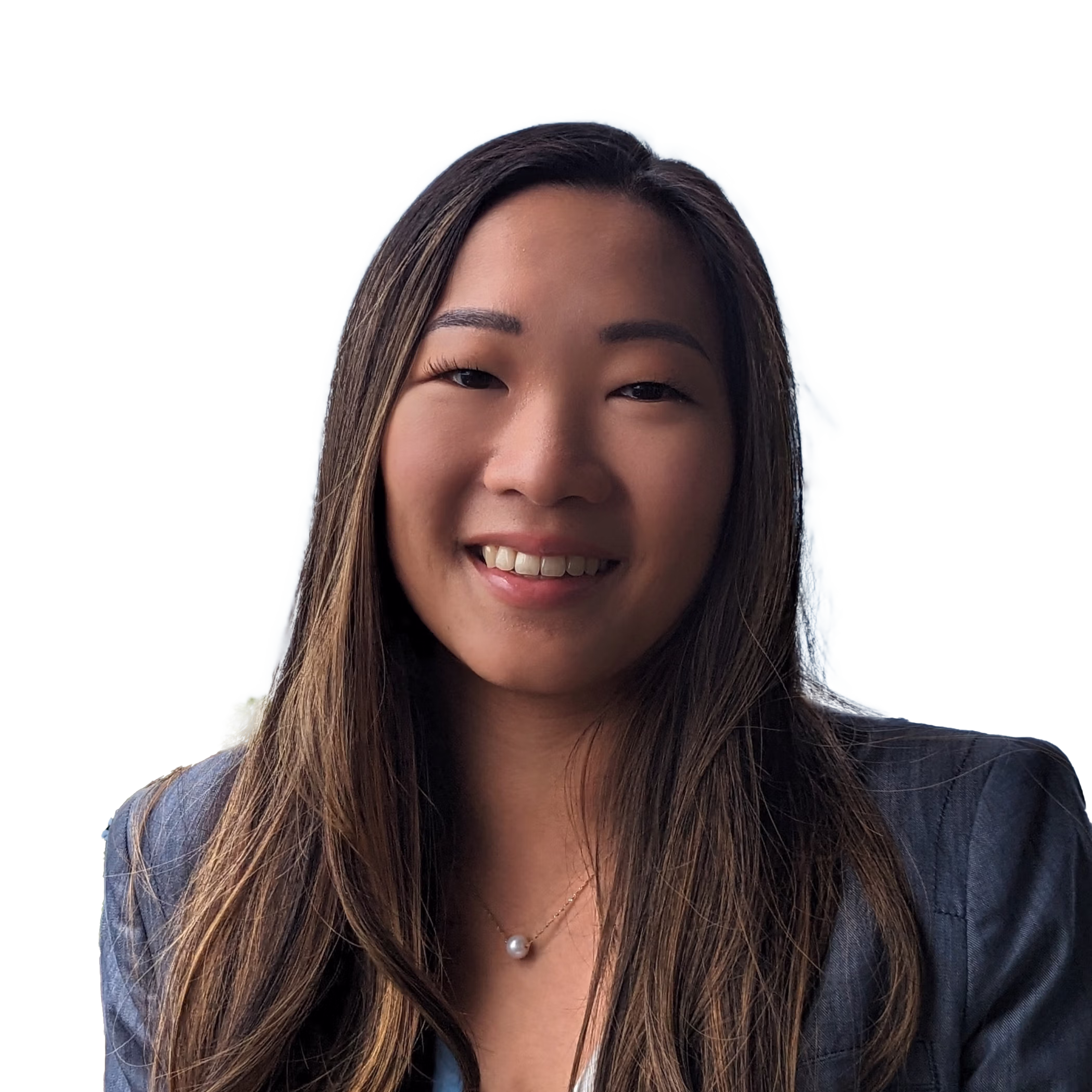 Smiling woman with long brown hair wearing a gray blazer and a pearl necklace against a light background.
