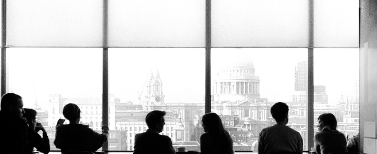 Silhouettes of six people sitting by a large window overlooking a cityscape with St. Paul's Cathedral in the background.