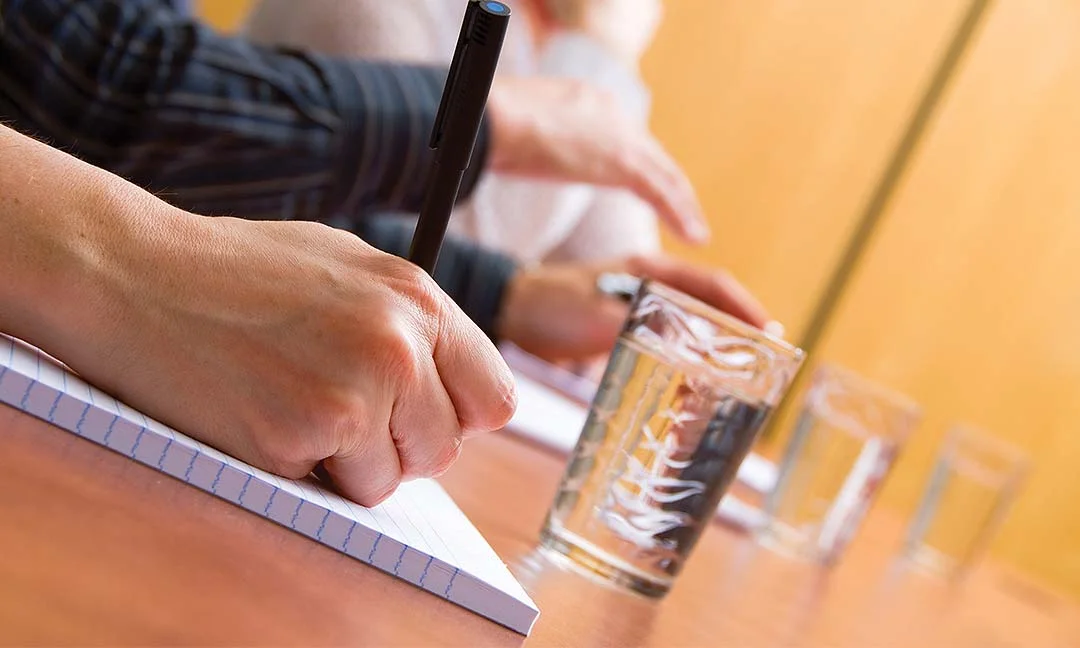 Person writing in a notebook beside glasses of water during a training course.