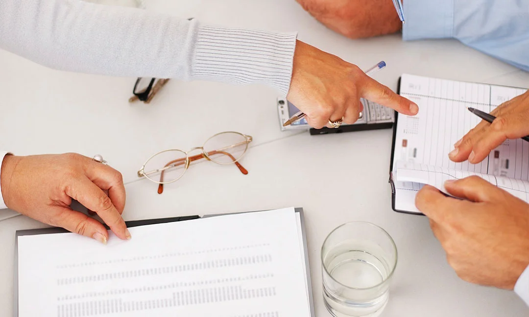 Hands pointing and writing on documents and planners during a technical discussion.