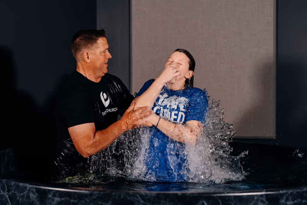 A woman baptizing a young girl in a baptismal pool, with water splashing around them.